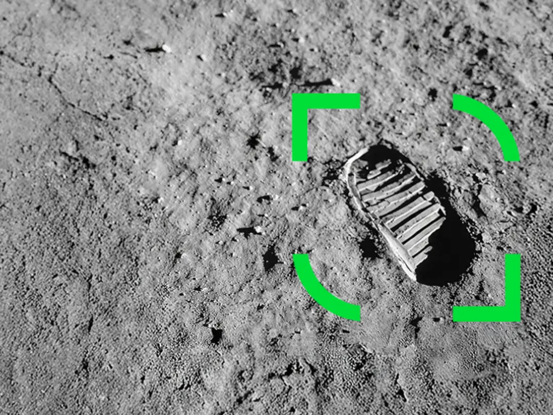 Fotspår på en sandig, grå yta markerat med en grön rektangel i mitten av bilden.